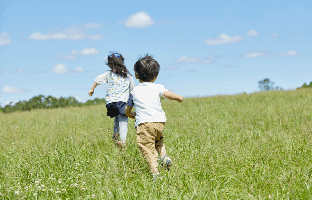 Two children running away from the camera in an open field