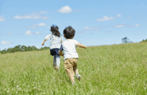 Two children running away from the camera in an open field